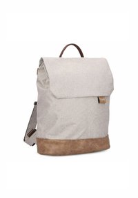 Mochila de lienzo en gris claro con fondo de cuero. Cuenta con un cierre de solapa, acentos marrones y un asa superior para un transporte fácil.