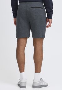 Graue Sweatshorts mit strukturierter Oberfläche, elastischem Bund und einer mit Reißverschluss versehenen Gesäßtasche, kombiniert mit grauen Sneakers und weißen Knöchelsocken.