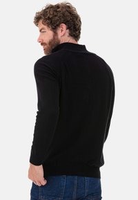Schwarzer Pullover mit langen Ärmeln, gerippten Bündchen und tailliertem Schnitt. Weiche Textur, einfache Verarbeitung, keine sichtbaren Muster oder Akzente.