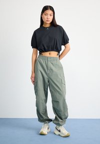 Black cropped t-shirt with round neckline and puffed sleeves. Olive green cargo pants with drawstring waist and multiple side pockets. Tan sneakers.