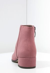 Stivaletto alla caviglia in suede rosa con tacco a blocco, punta arrotondata e dettaglio di cerniera laterale nascosta. Tessuto liscio e design minimalista.