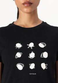 T-shirt noir arborant neuf illustrations blanches de coquillages et de créatures marines disposées en grille, avec "TOM TAILOR" imprimé en bas.