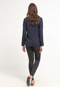 Blazer navy con design su misura, maniche lunghe e spacco posteriore, abbinato a jeans neri slim e sandali piatti. Finitura in tessuto liscio.