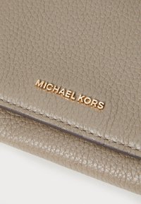 Portafoglio in pelle testurizzata grigio chiaro con logo dorato "MICHAEL KORS". Presenta un bordo liscio e una sottile lucentezza. Forma rettangolare compatta.