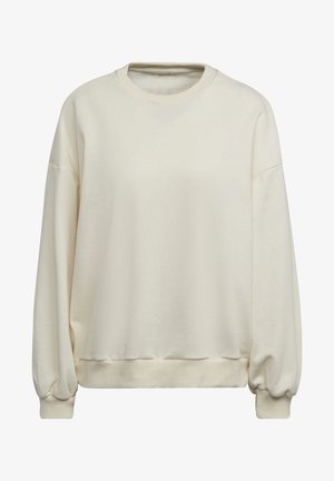 Vrouw met oversized, crèmekleurige sweatshirt en bijpassende broek met geribbelde boorden en zoom, haar dat naar de zijkant wappert.