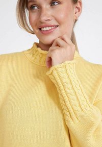 Gelber gestrickter Pullover mit hohem Rippkragen und strukturiertem Kabelmuster an den Ärmelabschlüssen. Weiches und leichtes Material.