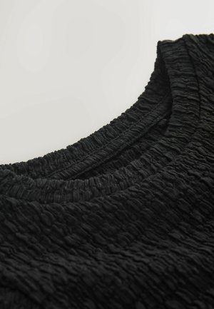 Čierna texturovaná látka s vrásčitým vzhľadom, s okrúhlym výstrihom a rebrovaným lemom. Detailný pohľad zvýrazňuje vzor materiálu.