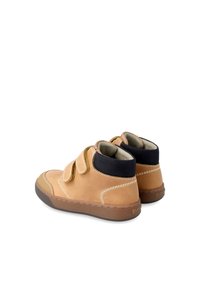 Bottes de cheville en daim beige avec des accents en textile noir, fermetures à bande Velcro, coutures contrastantes et semelles en caoutchouc marron.
