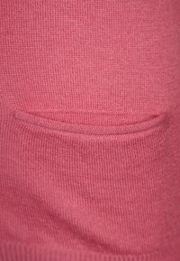 Lyserødt strikket stof med en lille, åben lomme nær bunden. Teksturen er blød med et ensartet ribbet mønster over det hele.