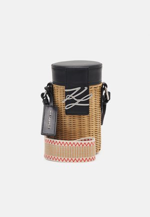 Cylindrisk vævet kurvetaske med sort lædertop, sølvlogo, sort mærke med teksten Karl Lagerfeld og beige rem med rødt zigzag-mønster.