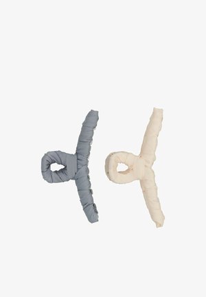 Accessori per capelli in tessuto morbido di colore grigio chiaro e rosa pallido, intrecciati a formare i simboli "%" e "d", con una finitura testurizzata.