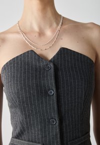 Rochie gri cu dungi fine, fără bretele, cu decolteu în V, două butoane închise la culoare și buzunare laterale. Accentuata cu coliere argintii stratificate.