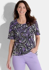 Kurzarmoberteil mit einem schwarz-lila-grauen wirbelnden Muster, runder Ausschnitt, kombiniert mit helllila Hosen. Glatte Stofftextur.