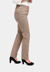 Braune, gerade geschnittene Jeans mit strukturiertem Finish und elastischem Bund. Schwarze Wildlederschuhe runden das Outfit ab.
