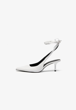 Valkoiset teräväkärkiset slingback-kengät, joissa on ohut nilkkahihna. Tasainen nahkamateriaali, ohut piikkikorko ja musta sisävuori.