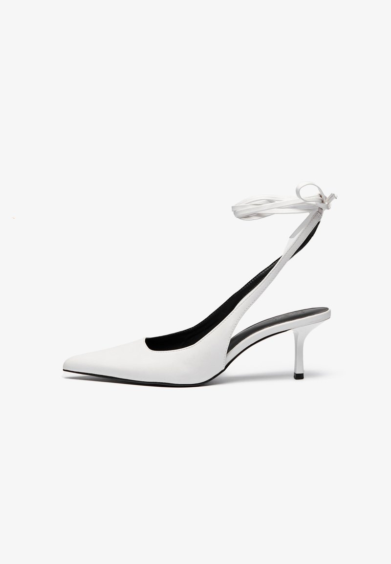 Valkoiset teräväkärkiset slingback-kengät, joissa on ohut nilkkahihna. Tasainen nahkamateriaali, ohut piikkikorko ja musta sisävuori.