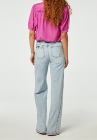 Lichtblauwe, hoge taille spijkerbroek met een recht model, voorzien van achterzakken. Gecombineerd met een roze blouse met korte mouwen.