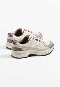 Sportovní boty v barvě krémové a šedé s texturovanou tkaninou, fialovými akcenty a polstrovanou podešví. Mají zaoblenou špičku a zesílenou oporu paty.