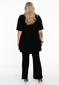 Zwarte tuniek met korte mouwen en een split aan de achterkant, gecombineerd met zwarte flared broek. Glad textuur, eenvoudig ontwerp en consistente kleur.