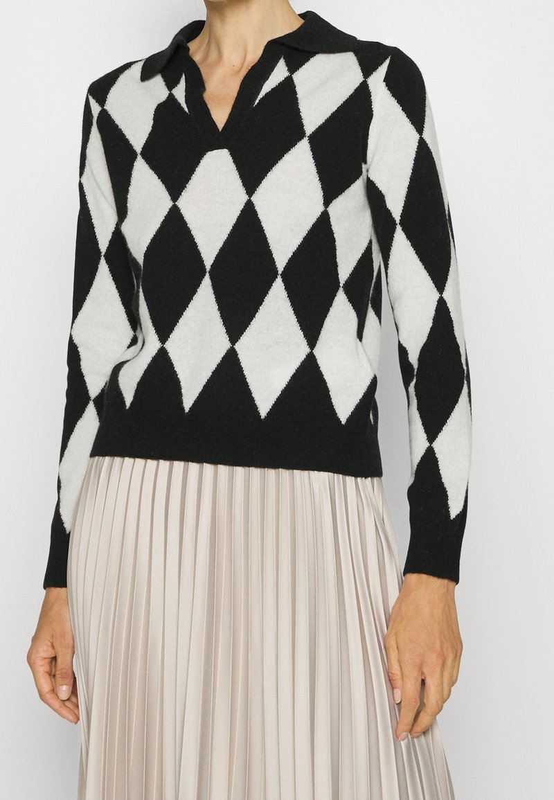Pull à motif losanges noir et blanc avec un col chemise, en tissu doux, associé à une jupe plissée beige.