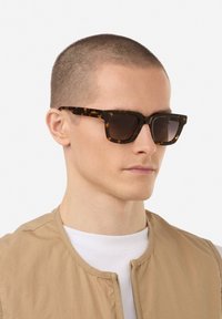 Ochelari de soare cu ramă pătrată în nuanța carapacei de țestoasă, lentile întunecate, finisaj mat și design minimalist.