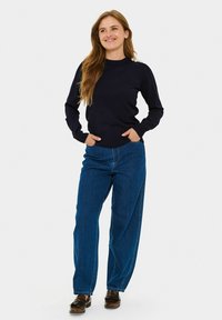 Granatowy sweter z okrągłym dekoltem z ozdobnymi akcentami na ramionach, zestawiony z luźnymi niebieskimi dżinsami i brązowymi mokasynami. Prosty design z prążkowanymi mankietami.