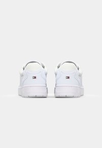 Paire de baskets basses blanches avec col rembourré et petit logo rectangulaire rouge, blanc et bleu sur la languette du talon.