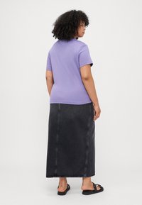 Lilla kortermet T-skjorte kombinert med et svart denim maxiskjørt. Skjørtet har synlig søm og en rett silhuett. Svarte sandaler fullfører antrekket.