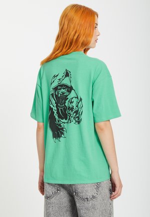 Groene katoenen t-shirt met een zwarte afbeelding van een brullende gorilla op de achterkant. Het ontwerp heeft een ontspannen pasvorm en korte mouwen.