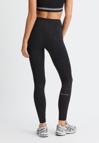 Leggings neri con un motivo geometrico, vita alta e un branding sobrio lungo il polpaccio, realizzati in un materiale elasticizzato e traspirante.