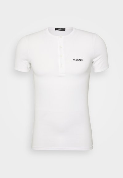Balta īsām piedurknēm T-krekls, izgatavots no ribotā kokvilnas, ar pogu plāksni un melnu izšūtu "VERSACE" logotipu uz krūtīm.