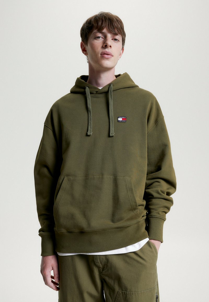 Olivenfarbener Kapuzenpullover aus Baumwollmischung mit einer frontalen Tasche und einem kleinen Logopatch. Rippbündchen und Saum.