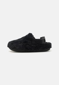 Svarta fluffiga tofflor gjorda av texturerat tyg med ett mjukt ytterlager och en gummisula. Har en slip-on design med en bakrem.
