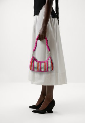 Personne portant un haut noir et une jupe blanche tenant un sac tissé multicolore avec une anse tressée rose, portant des talons pointus noirs.