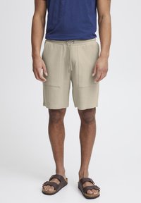 Shorts bej cu textură, cu un talie elastică și �șnur, având două buzunare frontale. Purtați cu sandale maro.