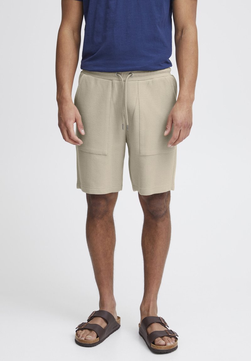 Beige, teksturerte shorts med elastisk midjebånd og snor, med to frontlommer. Brukt med brune sandaler.