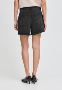 Shorts en denim noir avec une taille haute et un ourlet effiloché. Présente deux poches arrière et un aspect texturé. Assortis avec des chaussures noires.