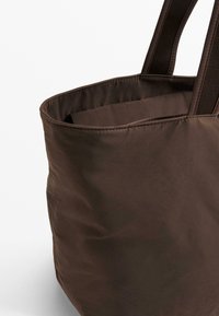 Dark brown tote bag made of nylon with a soft texture. Features two sturdy fabric handles and a rounded, slouchy shape.