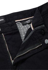 Úzké černé kalhoty s částečně otev řeným zipem, knoflíkem a viditelnou vnitřní štítkem se značkou "KAITO."