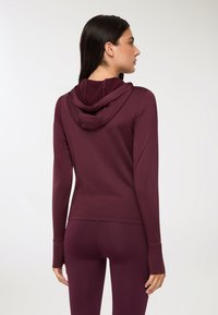 Hoodie a maniche lunghe color bordeaux con una vestibilità rilassata, caratterizzato da un cappuccio a doppio strato e fori per i pollici nelle maniche. Tessuto morbido e elastico.