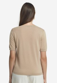 Beige kortærmet sweater med rund halsudskæring, glat strikket tekstur og ribbede manchetter, der viser et enkelt, tætsiddende design.