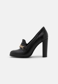 Scarpa nera in pelle con tacco alto, punta tonda e un accento in catena dorata sulla tomaia. Caratterizzata da una texture liscia e un robusto tacco a blocco.