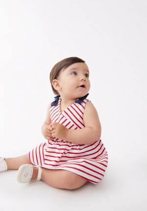 Vestido a rayas con líneas horizontales en rojo y blanco, con un escote en V y un cuello de color azul marino. Tejido suave, diseño sin mangas y zapatos blancos.