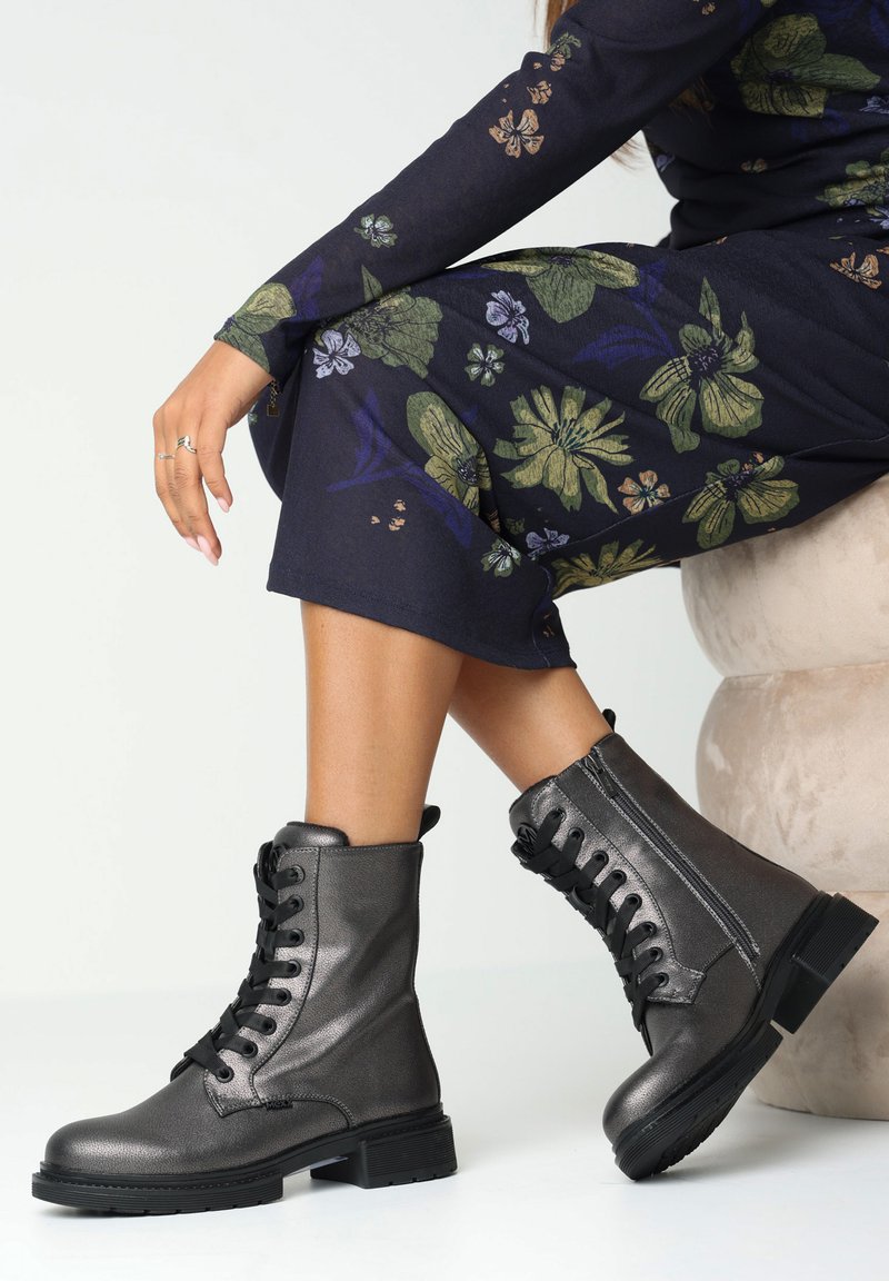 Metalické šedé kotníkové boty na šněrování s kulatou špičkou, texturovaným koženým povrchem a silnou černou podrážkou.