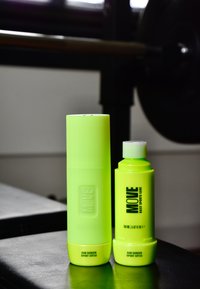 Dwie jaskrawe zielono-żółte butelki z filtrem przeciwsłonecznym o żłobionych i gładkich powierzchniach; jedna wysoka i cylindryczna, a druga krótsza i szersza, obie oznaczone etykietami.