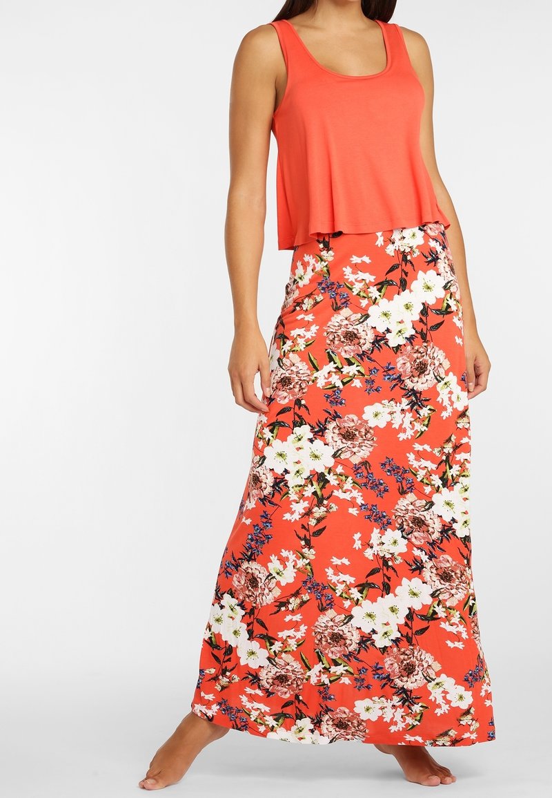 Débardeur corail à la coupe fluide associé à une longue jupe fleurie ornée de grandes fleurs blanches, roses et bleues sur un fond vibrant.