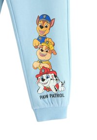 Helle blaue Sweatpants mit drei Cartoon-Hundfiguren aus "Paw Patrol", die an der Seite aufgedruckt sind, in lebendigen Farben und detaillierten Designs.
