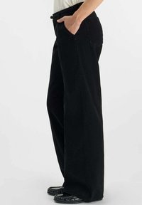 Los pantalones anchos negros cuentan con bolsillos laterales y una superficie texturizada. Combinados con unas bailarinas negras, el conjunto se complementa con una blusa clara.