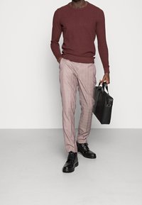 Maglione a maglia color marrone, pantaloni a scacchi rosa chiaro, stivaletti neri alla caviglia e una valigetta in pelle nera. Texture morbide e design aderente.