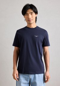 Ναυτ�ικό μπλε βαμβακερό μπλουζάκι με κοντά μανίκια, στρογγυλή λαιμόκοψη και μικρό λευκό λογότυπο στο στήθος. Λείο ύφασμα, χαλαρή εφαρμογή.